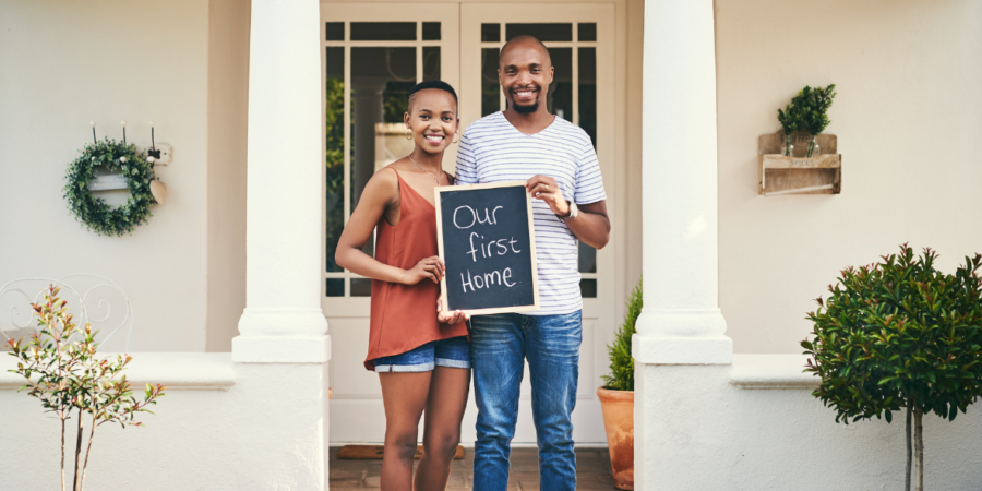 young couple outside of first home with chalkboard sign