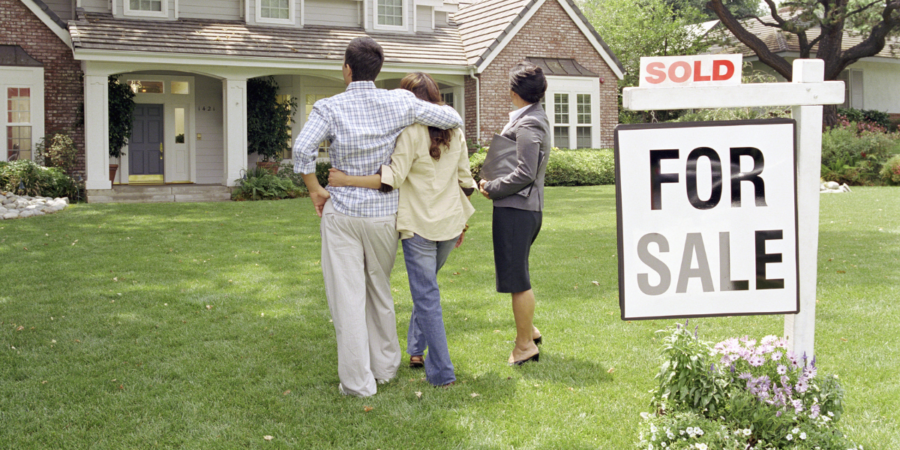 family outside home with realtor and for sale sign